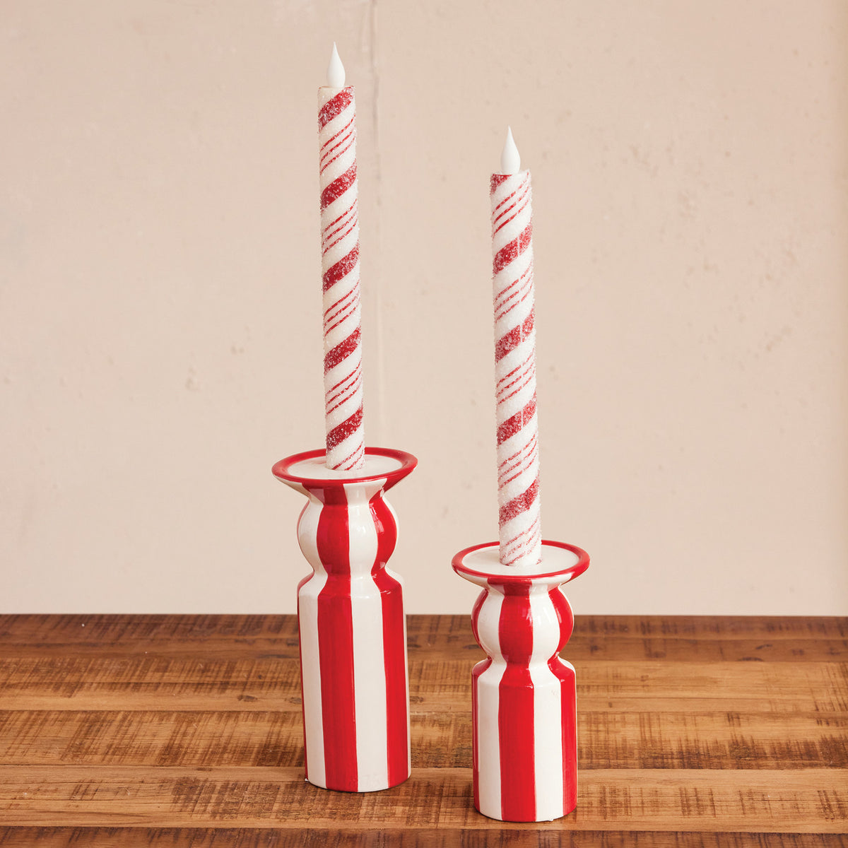 Two hand-painted red and white striped ceramic taper holders with matching candy cane candles.
