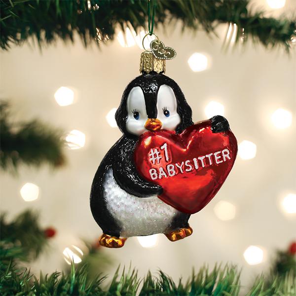 Penguin ornament holding a red heart that says #1 BABYSITTER hanging on a Christmas tree.