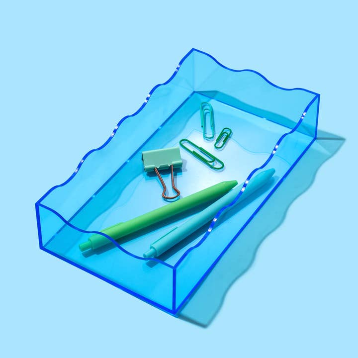 Small blue wavy acrylic rectangle tray containing pens and paperclips on a light blue background.