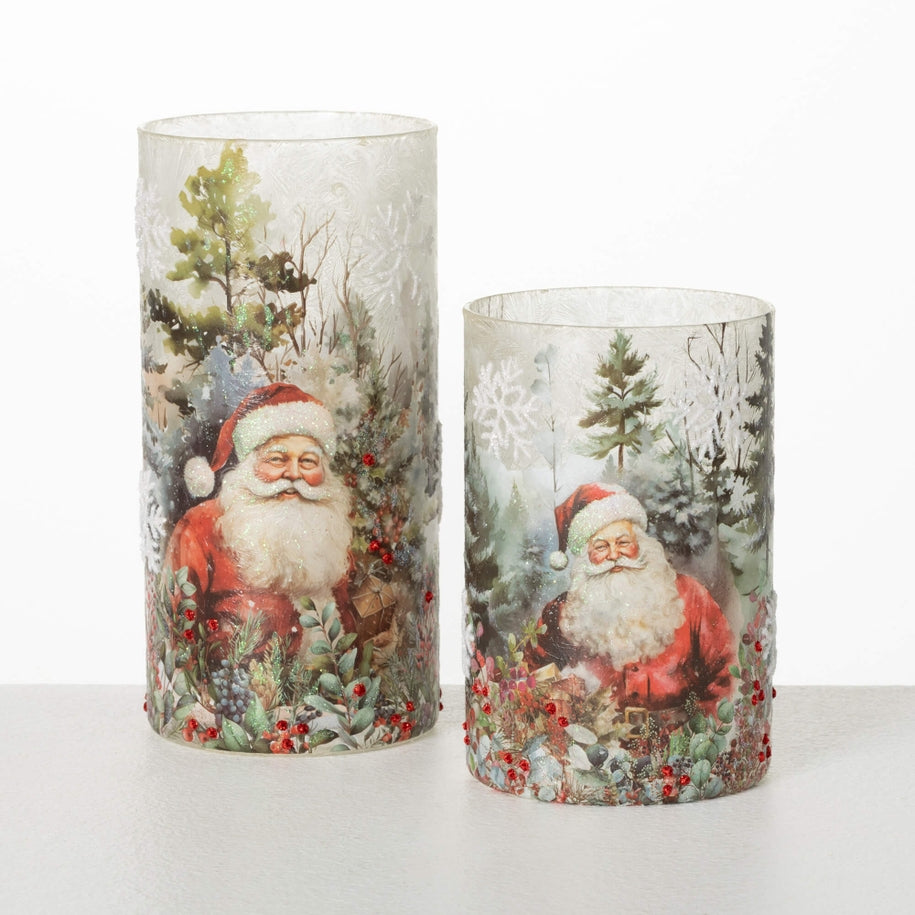 Two cylindrical glass Santa candleholders with vintage-style illustrations and red bead accents.