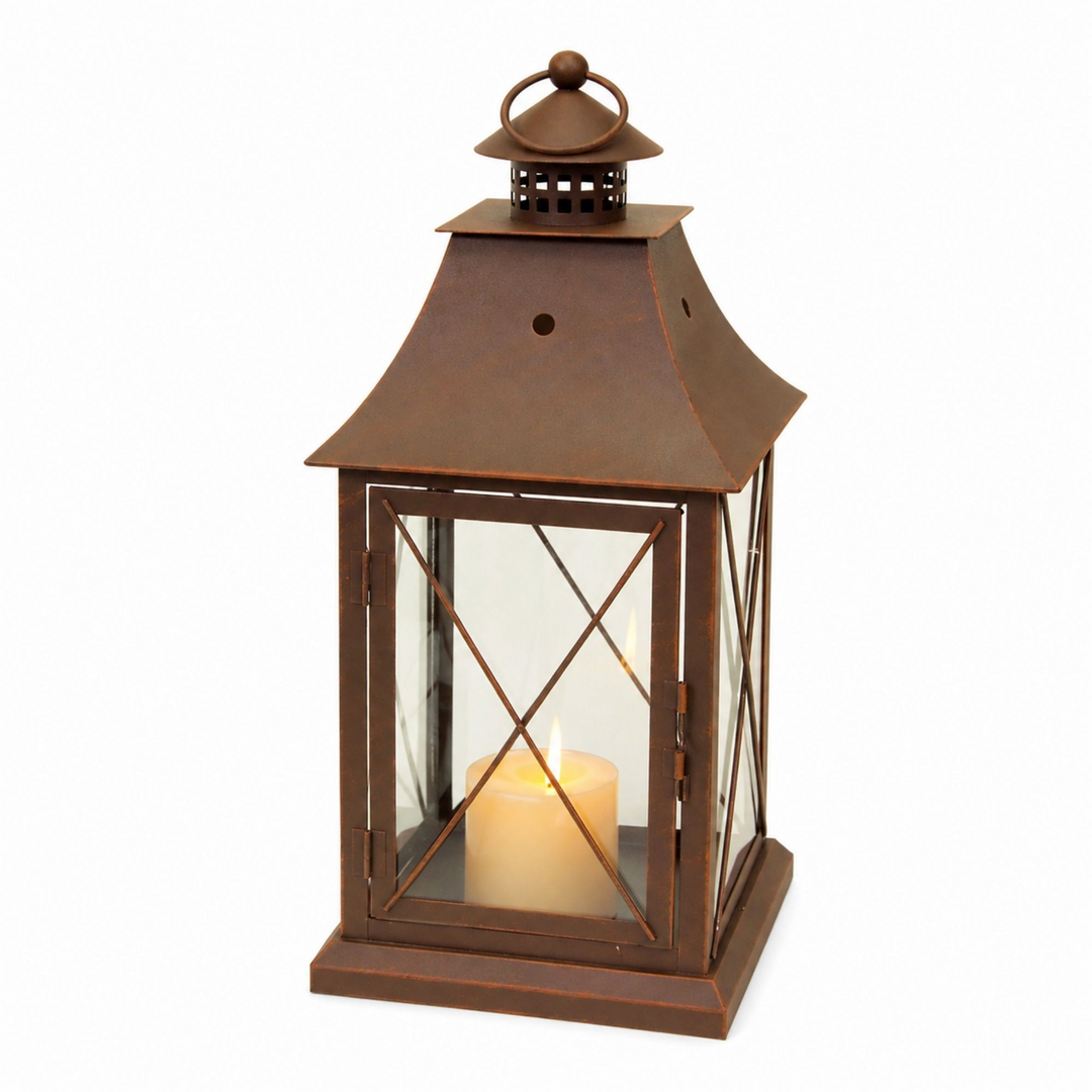 Rustic brown metal lantern with a lit pillar candle inside, featuring a classic X-frame design.