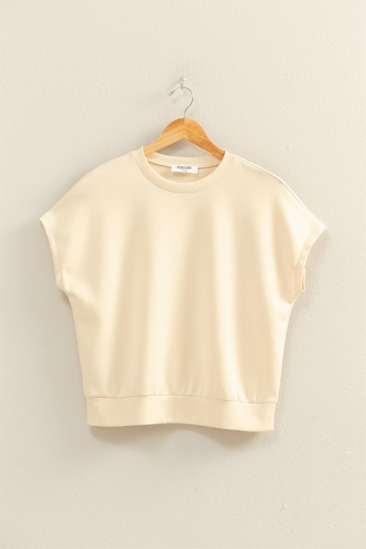 Cream-colored Alecia crew neck top with short dolman sleeves hanging on a wooden hanger.