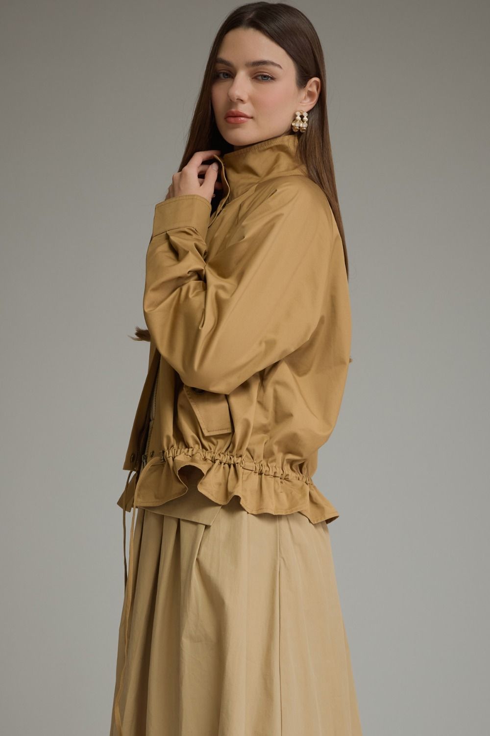 Woman wearing the Andrea Solid Long Sleeve Jacket in tan with a ruffled hem and high collar.