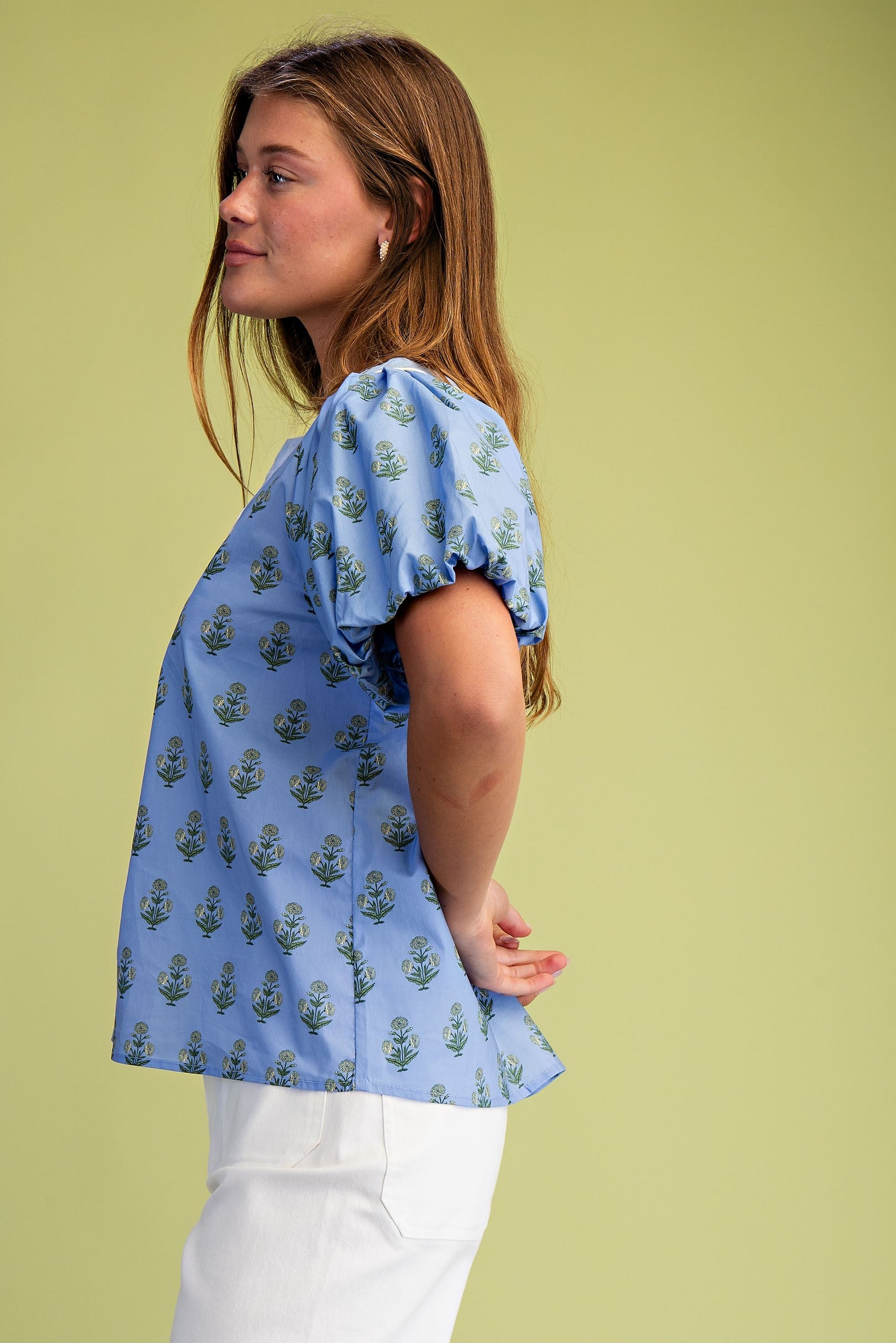 Side view of a woman wearing a blue floral notch neck blouse with short puff sleeves and white pants