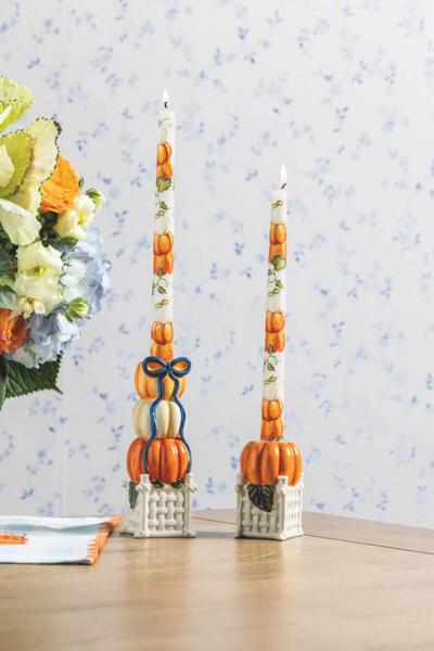 Two hand-painted pumpkin topiary taper candle holders on a wooden table with lit candles.