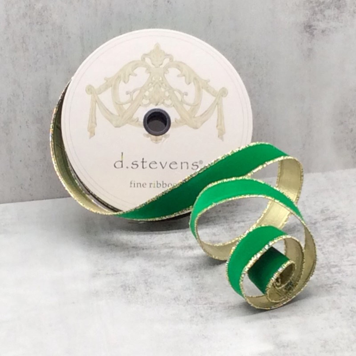 A spool of green flocked velvet ribbon with metallic gold backing and gold-trimmed edges.