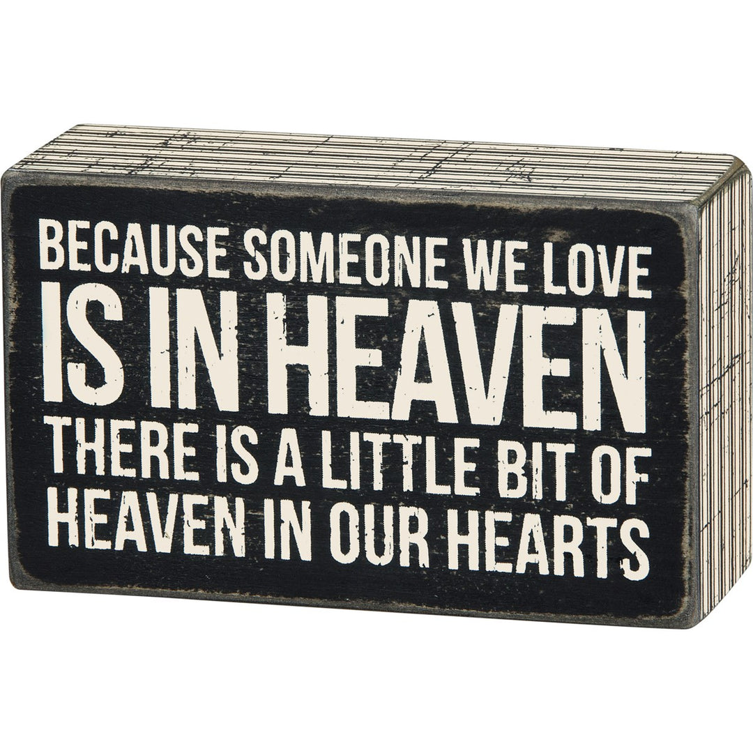 Black wooden box sign with white text reading 'Because someone we love is in heaven, there is a little bit of heaven in our hearts.'