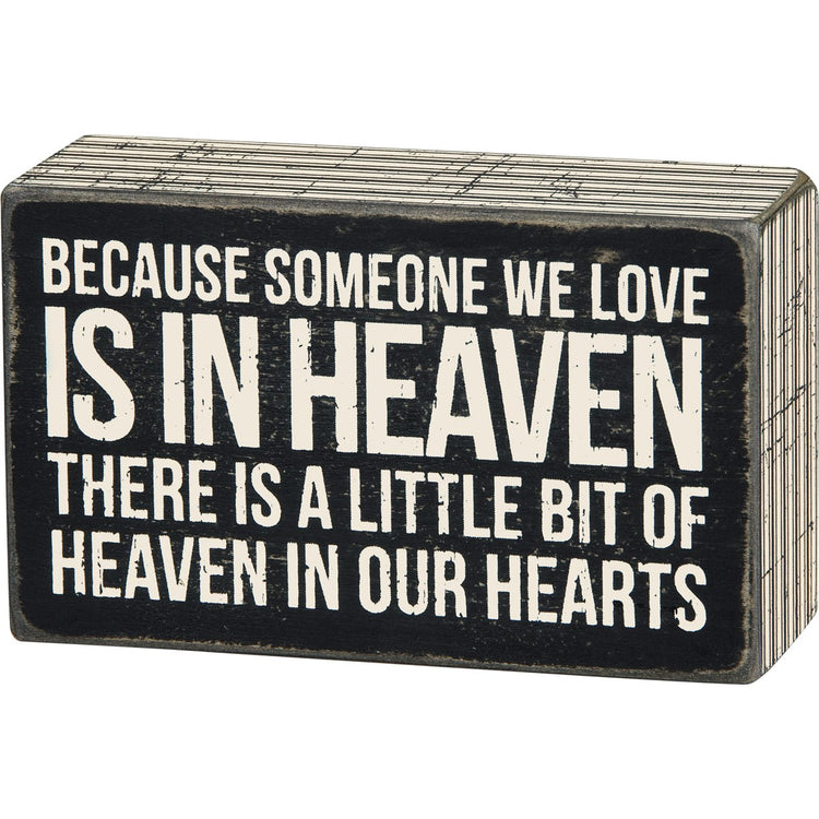 Black wooden box sign with white text reading 'Because someone we love is in heaven, there is a little bit of heaven in our hearts.'