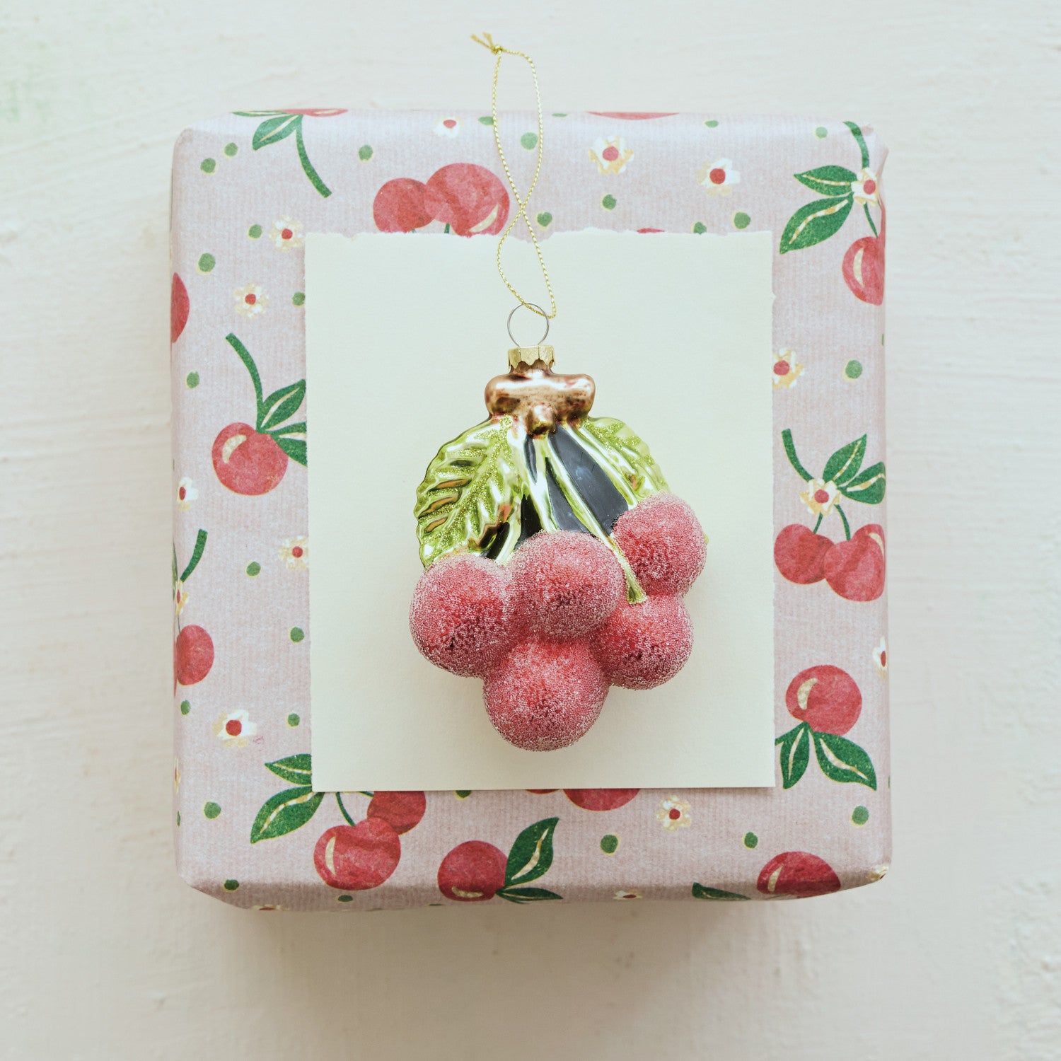 Red sugared glass cherry cluster ornament with green leaves on a cherry-patterned gift box.