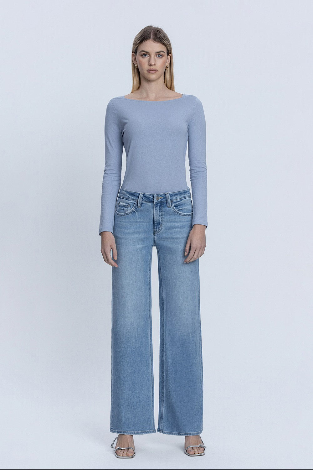 Woman wearing Natalie mid-rise full length medium wash wide leg jeans and a blue long sleeve top.