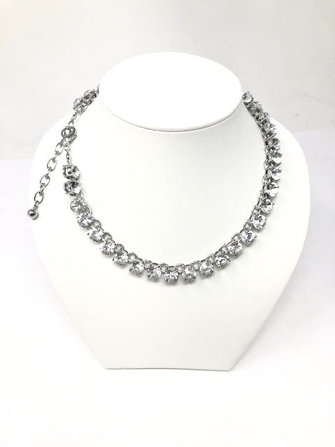 Silver tone tennis necklace with round clear crystals on a white jewelry display stand.