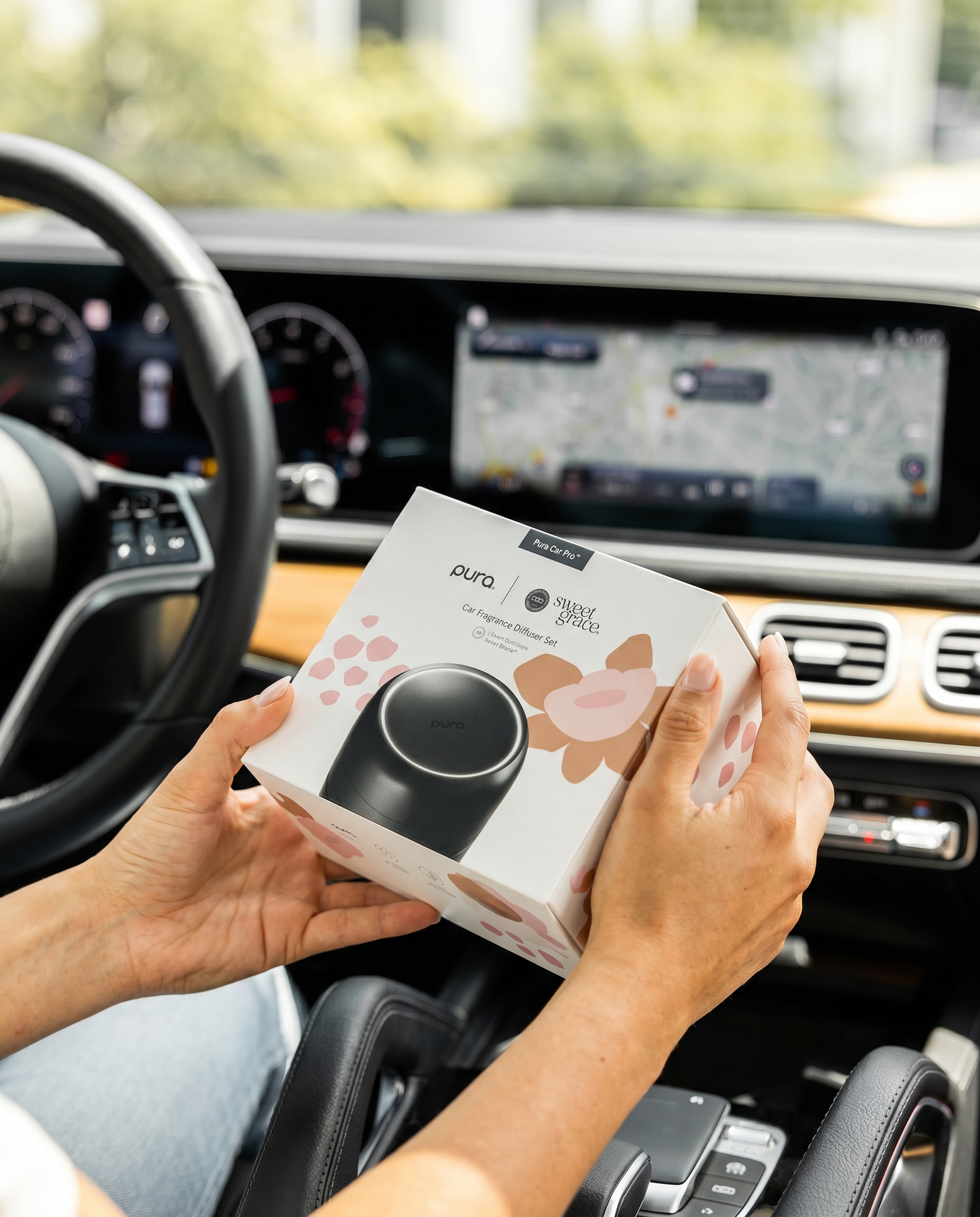 Hands holding a Pura Sweet Grace Car PRO Diffuser Set box inside a car interior.