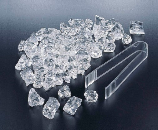 A pile of clear acrylic display ice chips next to a pair of clear plastic tongs.