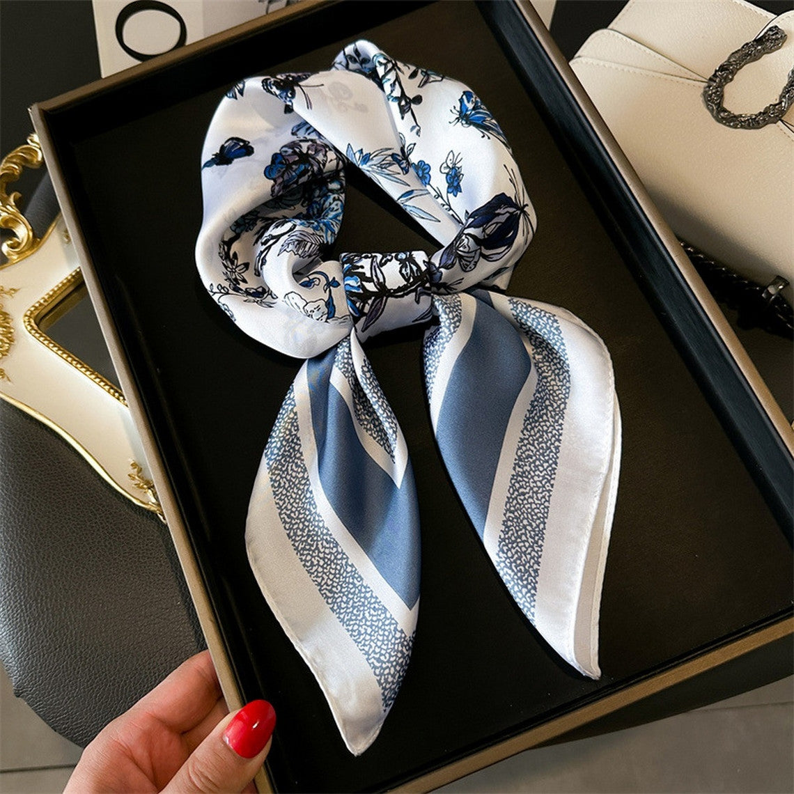 Silky white scarf with blue butterfly and floral prints, tied in a bow on a black tray.