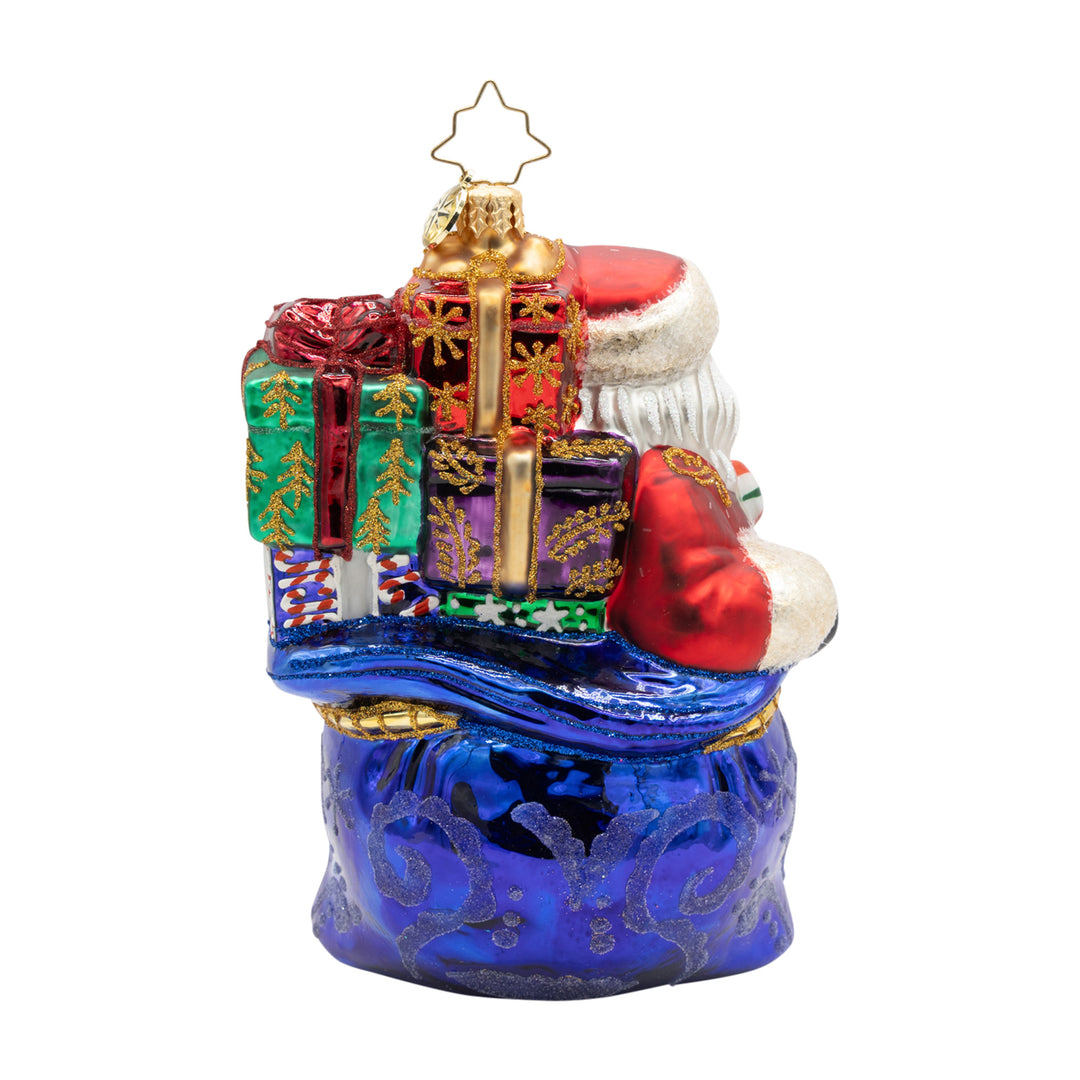Kris Kringle’s Bundle glass ornament featuring Santa with a blue sack and colorful gifts.