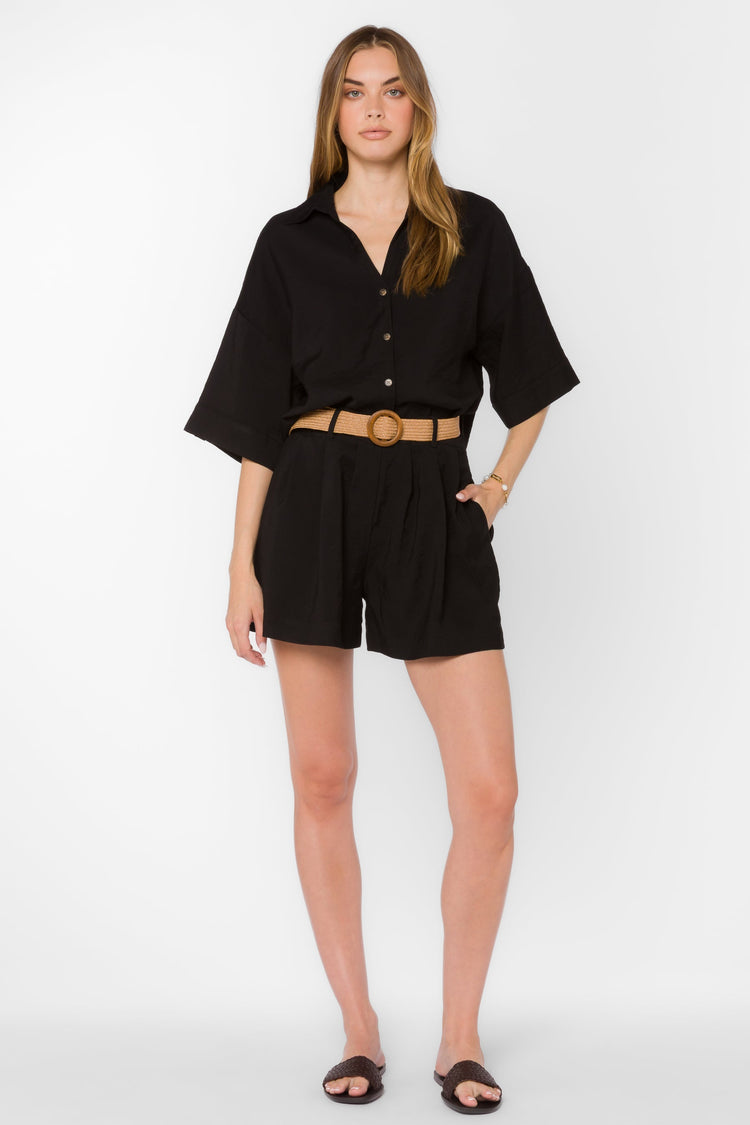 Woman wearing black high-waisted Lynette Shorts with front pleats and a tan woven belt.