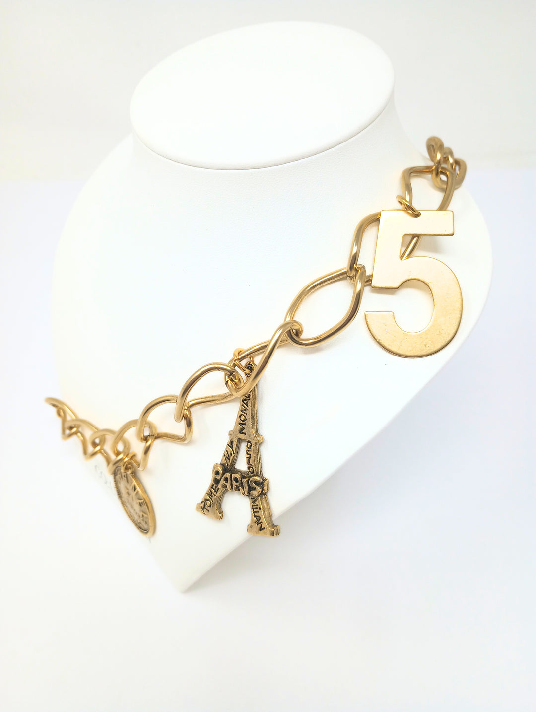 Gold link necklace featuring five charms: Paris heart, Eiffel Tower, number five, and two Chanel-style coins.