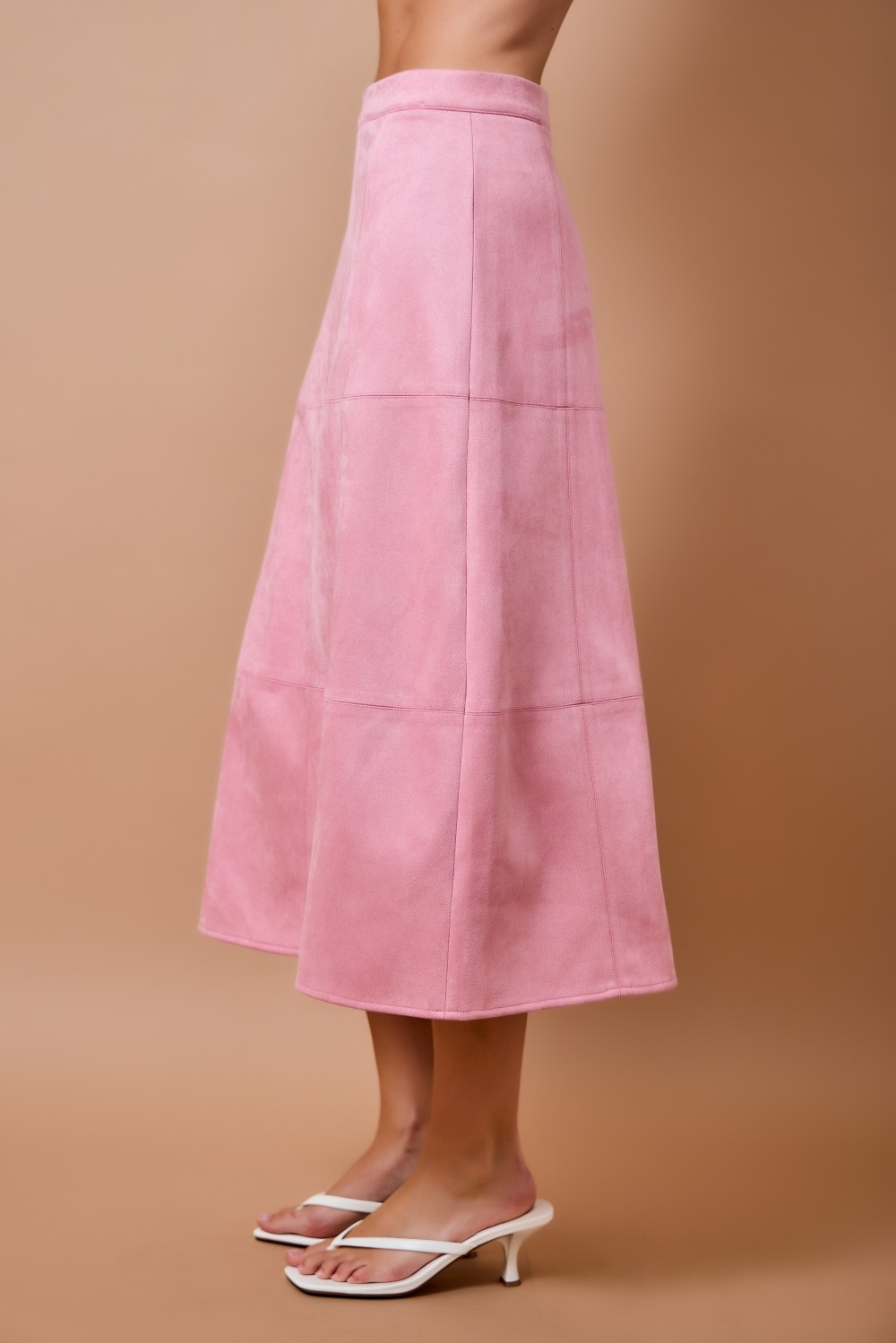 Side view of a pink high-waisted suede A-line midi skirt with panel seam detailing.
