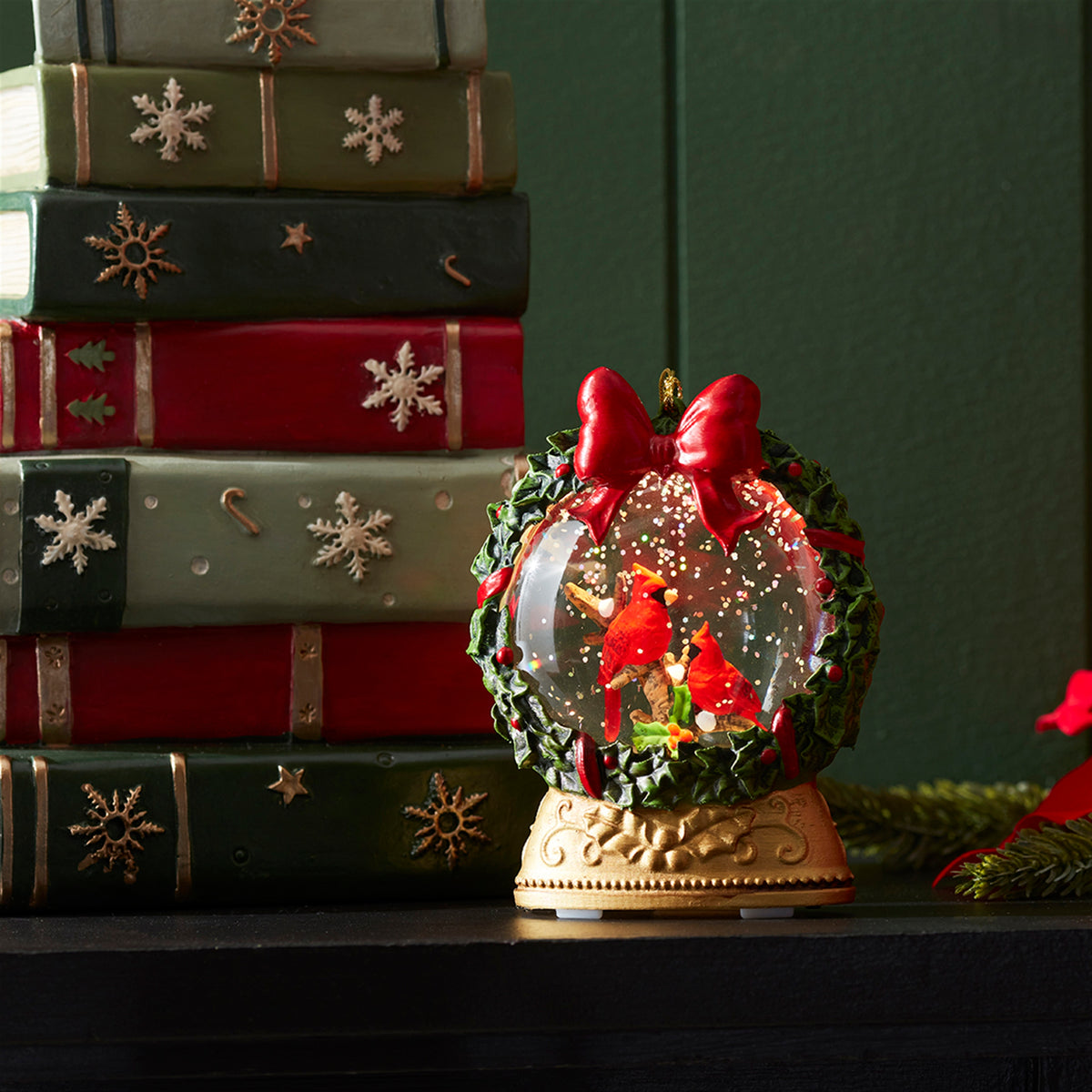 LED Globe Ornament with red cardinals inside a wreath, set against a stack of decorative books.
