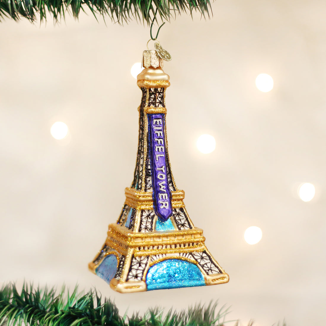 Eiffel Tower glass Christmas ornament with gold glitter and blue accents hanging on a tree.