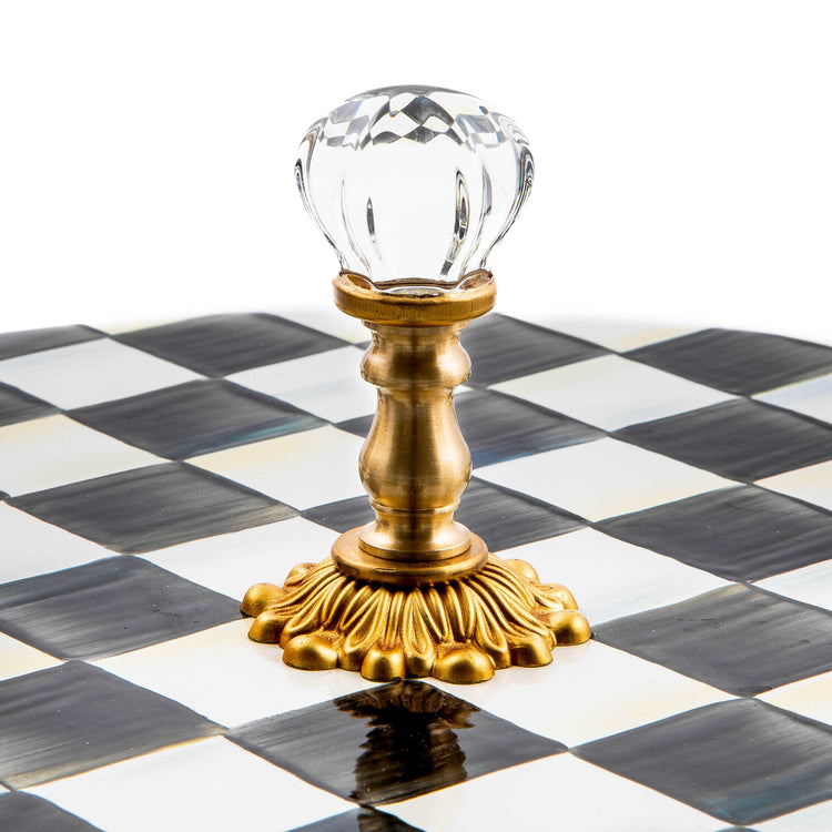 Close-up of a crystal knob on an antiqued brass-plated stand atop a black and white checkered plate.