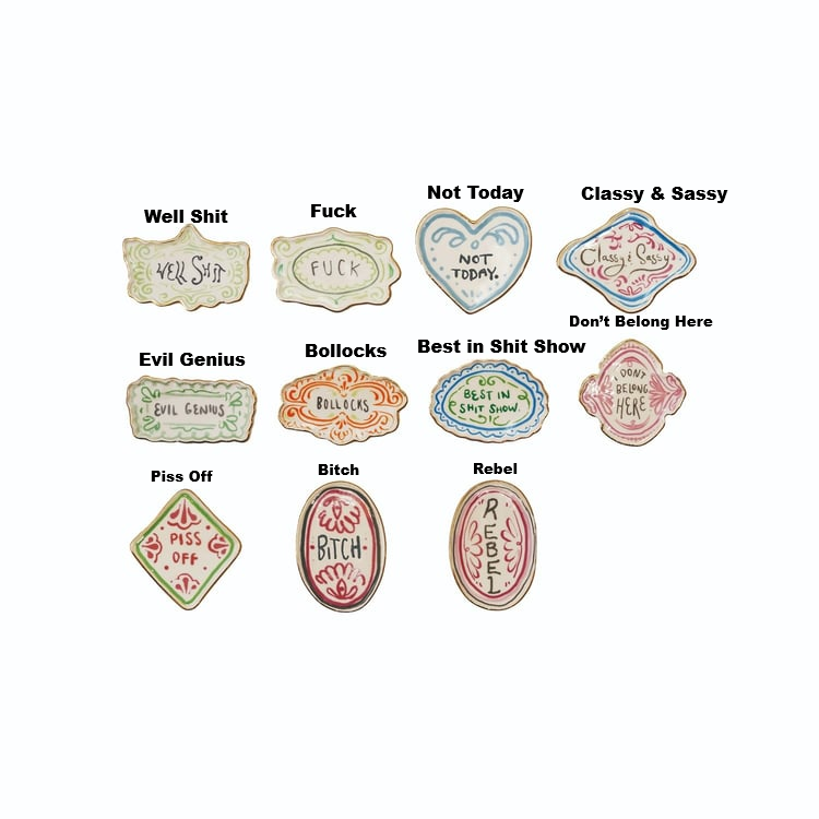 Assorted stoneware magnets with electroplated edges and humorous phrases in various shapes.