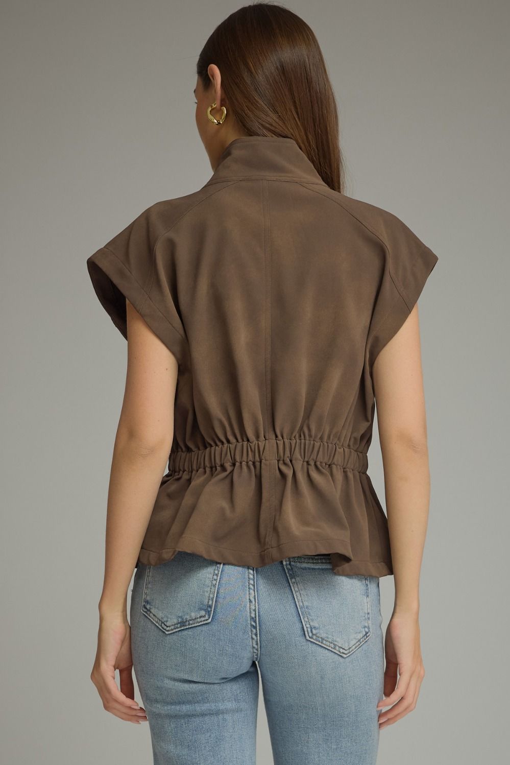 Back view of a woman wearing a brown Sarah Solid Cap Sleeve Jacket with an elastic waist and jeans.