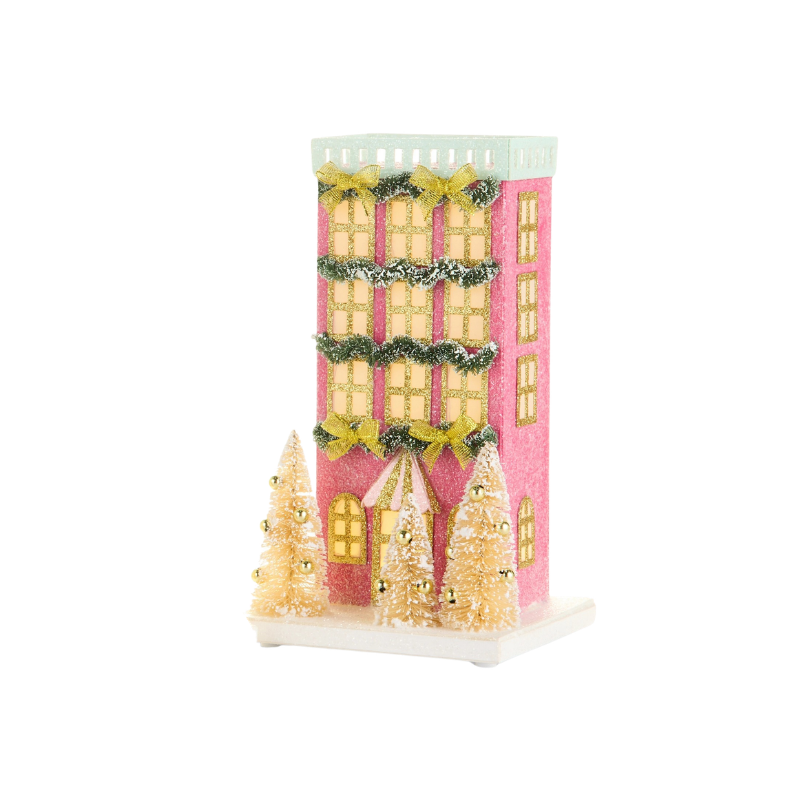 Lighted pink paper house with gold windows, green garlands, bows, and three sisal trees on a base.