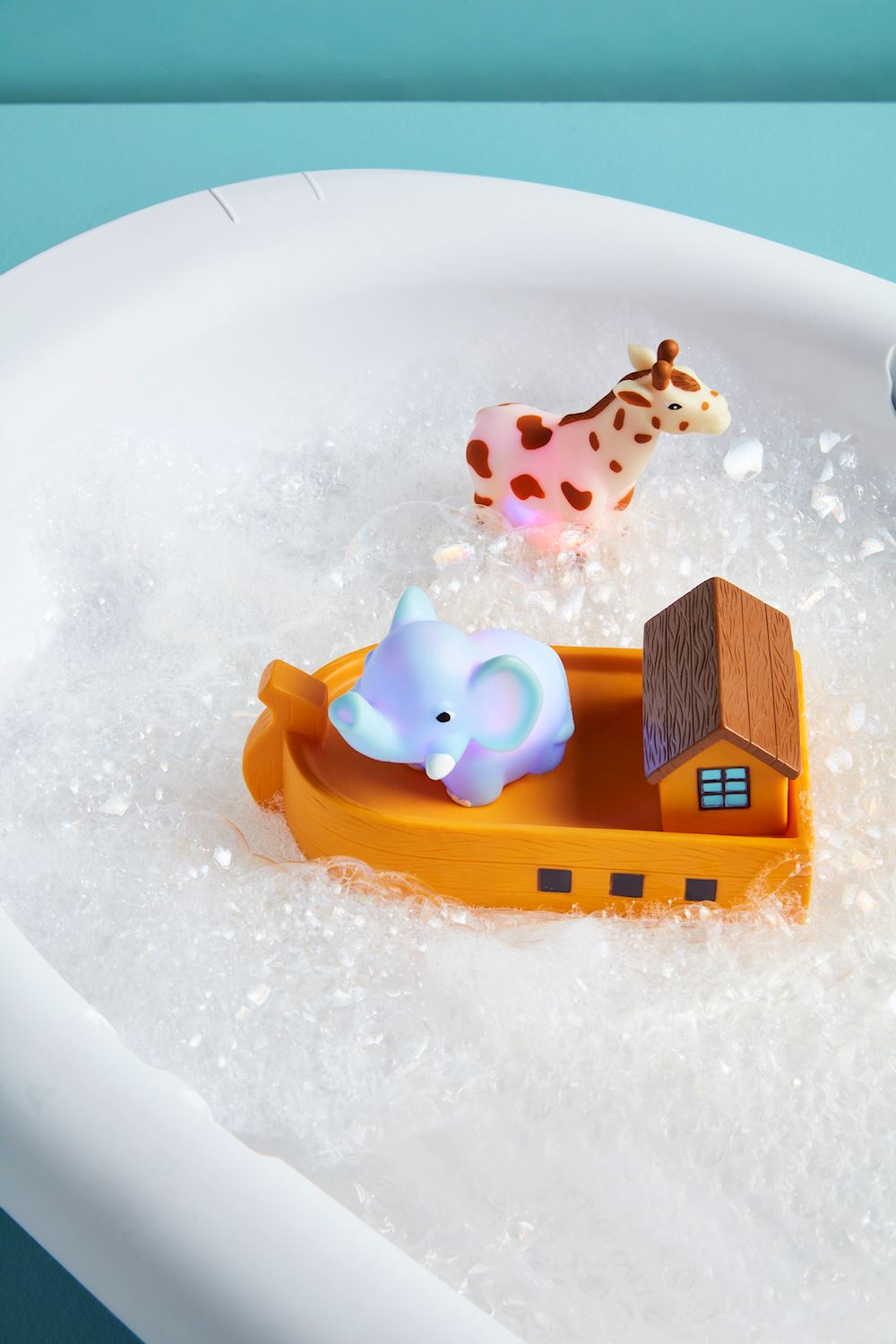 Light-up rubber elephant and giraffe bath toys on an orange toy ark in a bubbly bathtub.