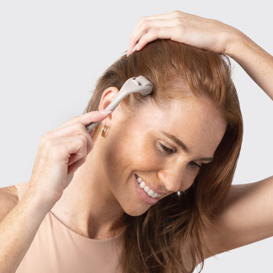 A woman uses a warm gray Micro Derma Facial Roller on her scalp near the hairline.
