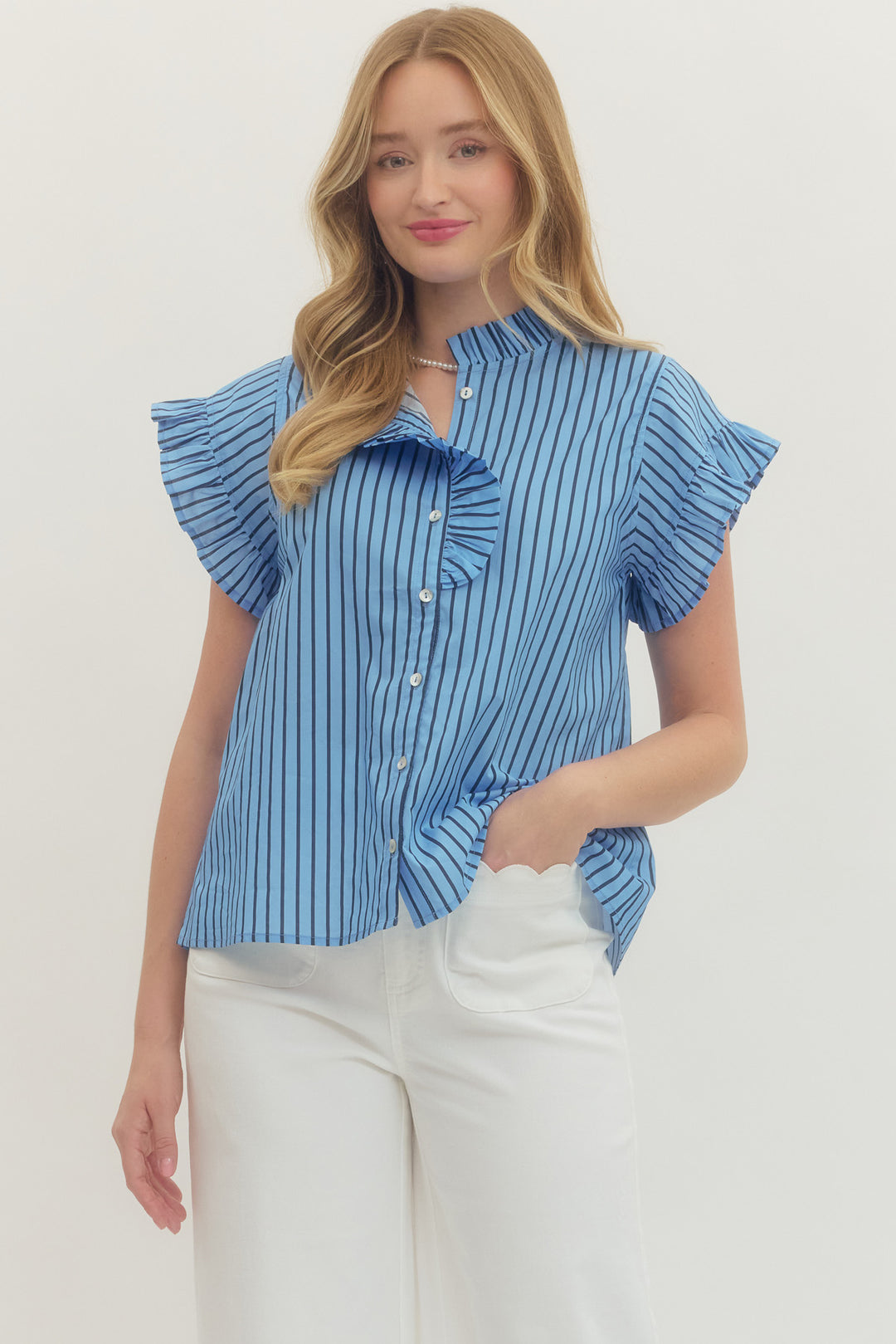 Woman wearing the Rhea blue and white striped short sleeve top with ruffle details and white pants.