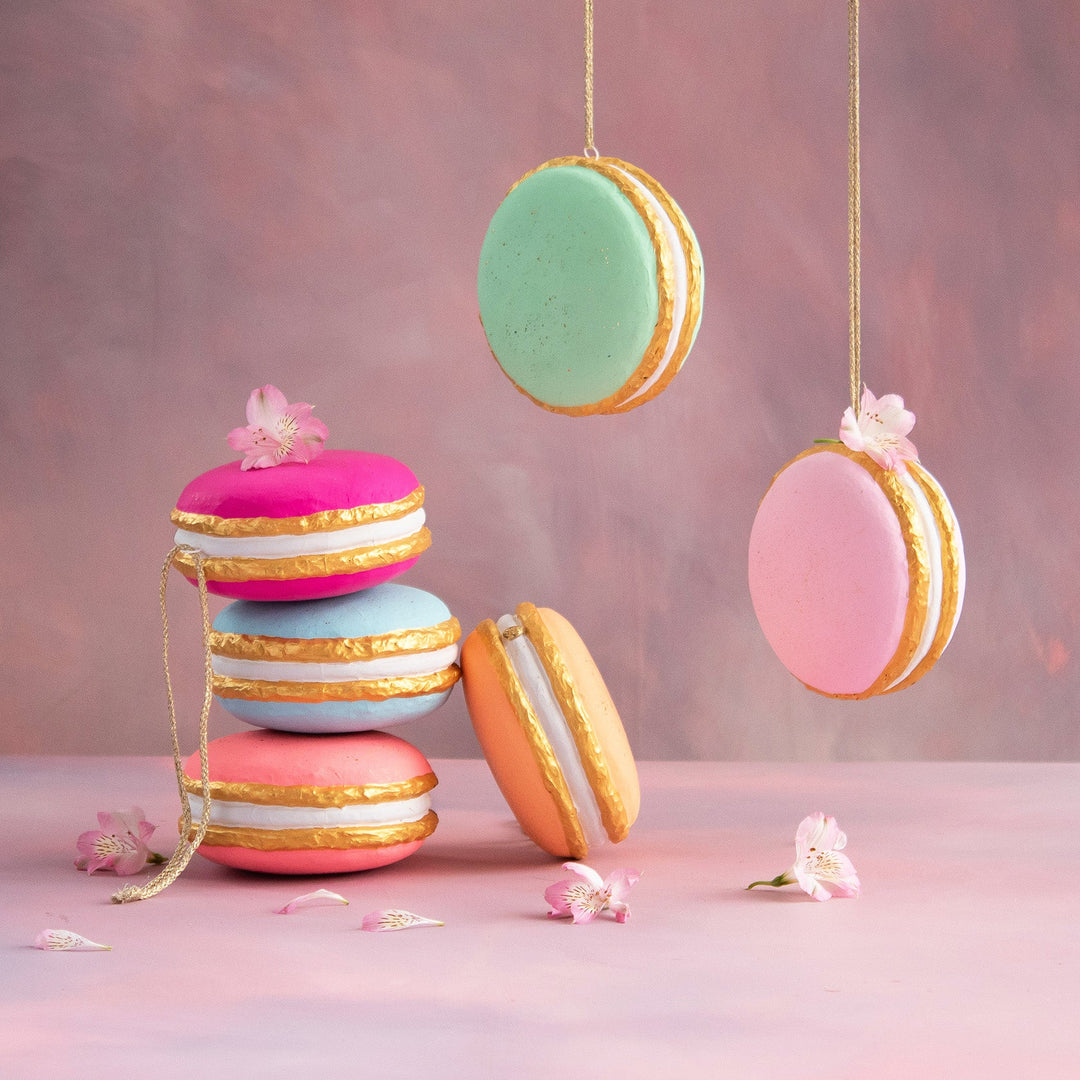 Hand-painted fiber pulp macaron ornaments in pastel colors with gold leaf accents and floral detail.