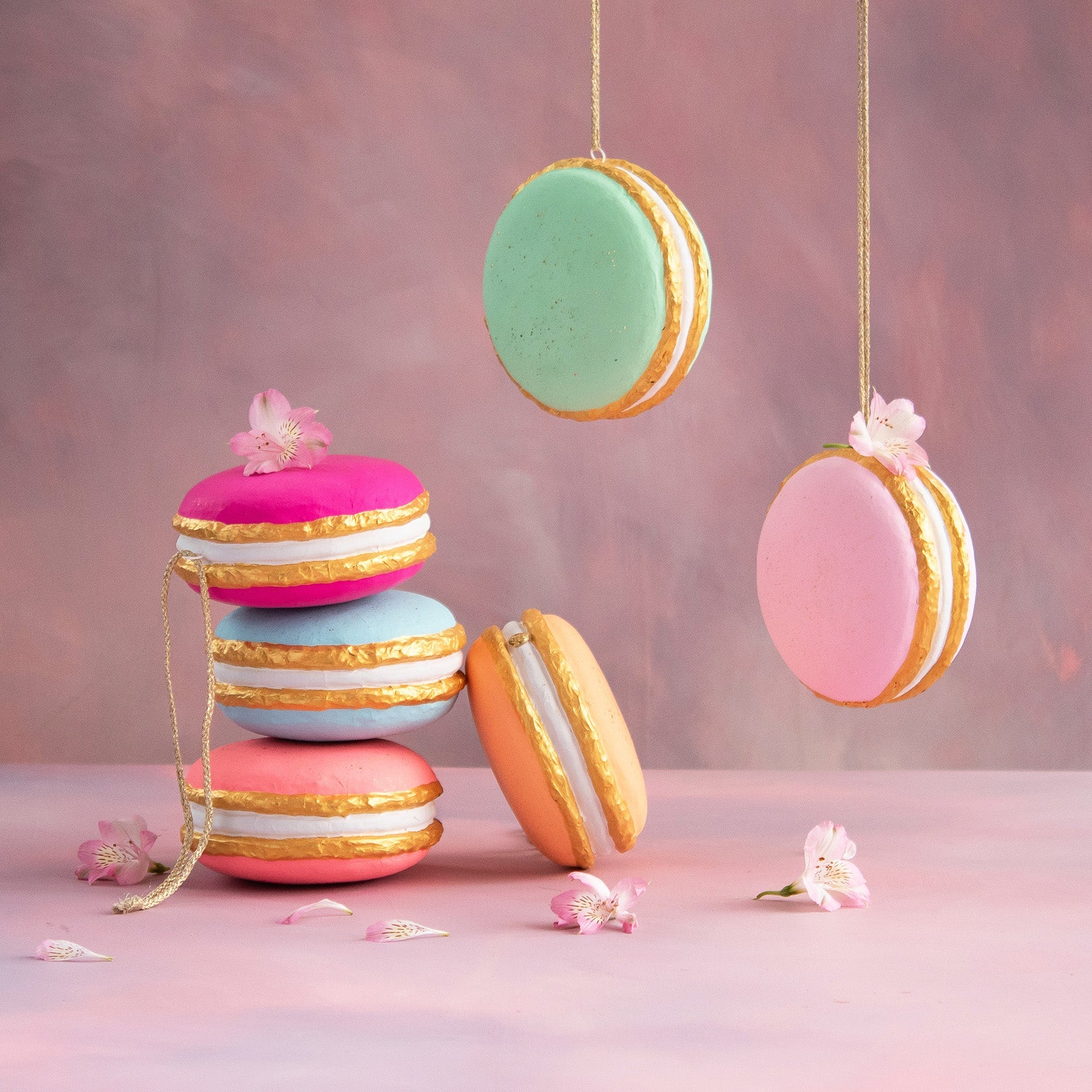 Hand-painted fiber pulp macaron ornaments in pastel colors with gold leaf accents and floral detail.