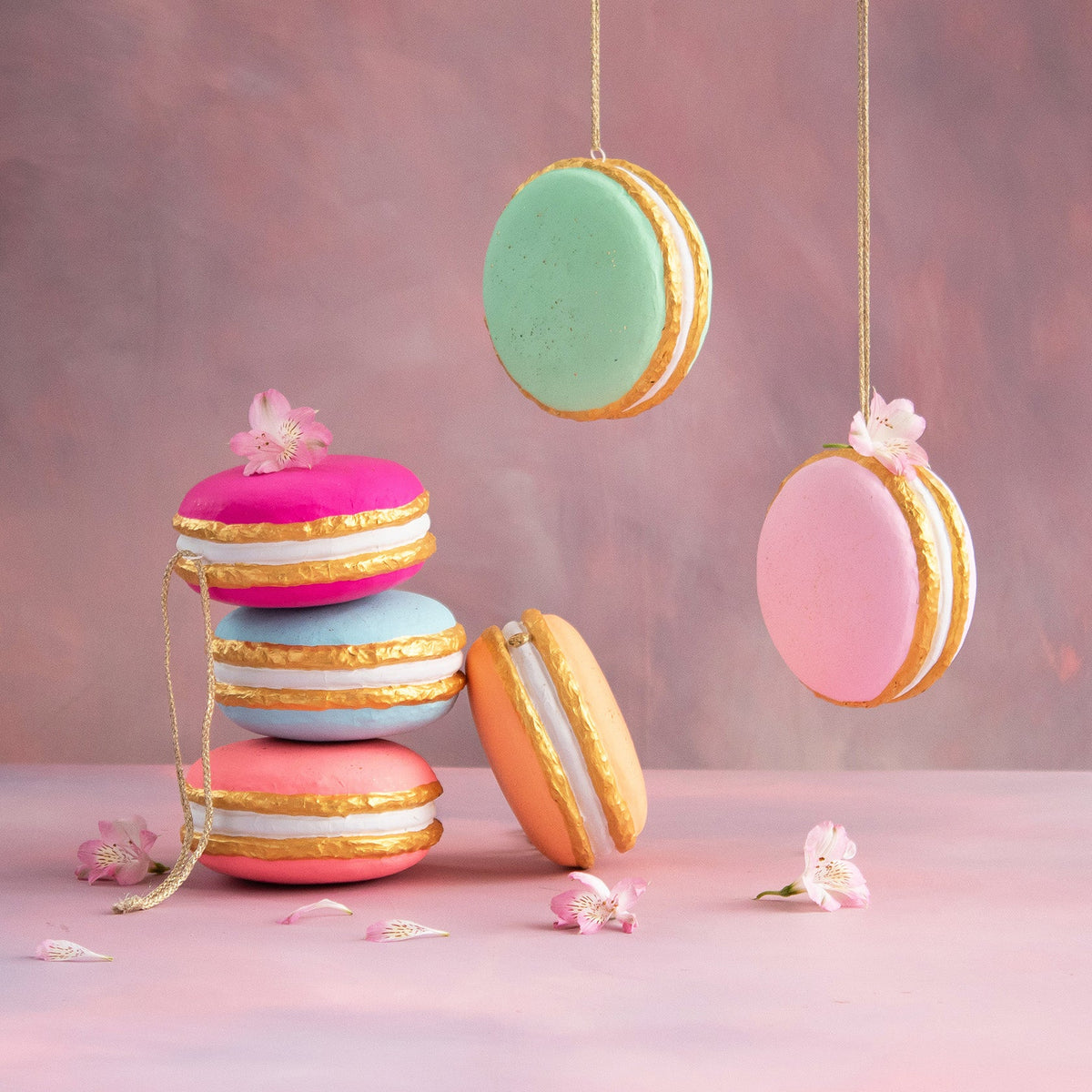 Hand-painted fiber pulp macaron ornaments in pastel colors with gold leaf accents and floral detail.