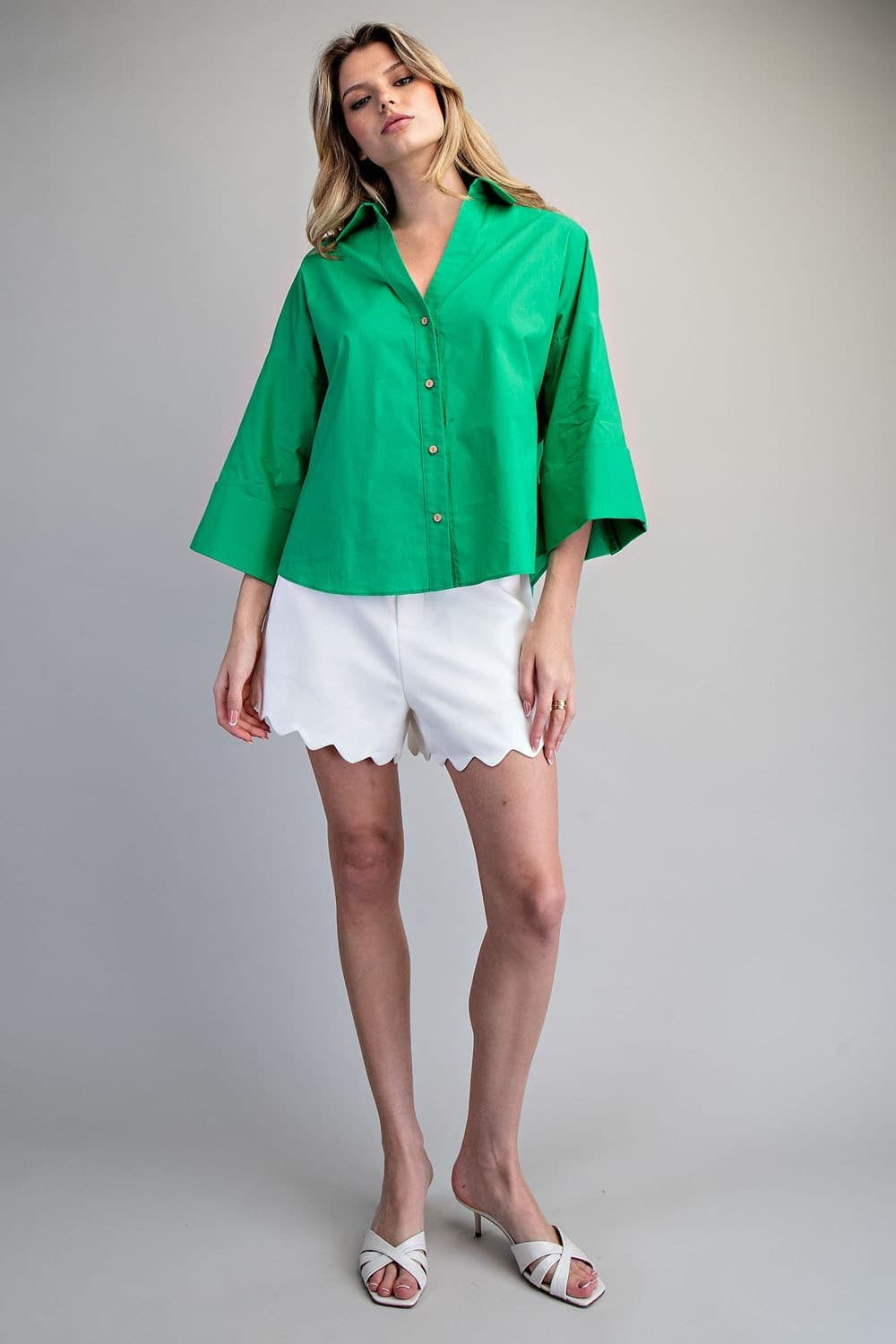 Woman wearing a green Blake Back Pleat Button Down Blouse Top with white scalloped shorts.