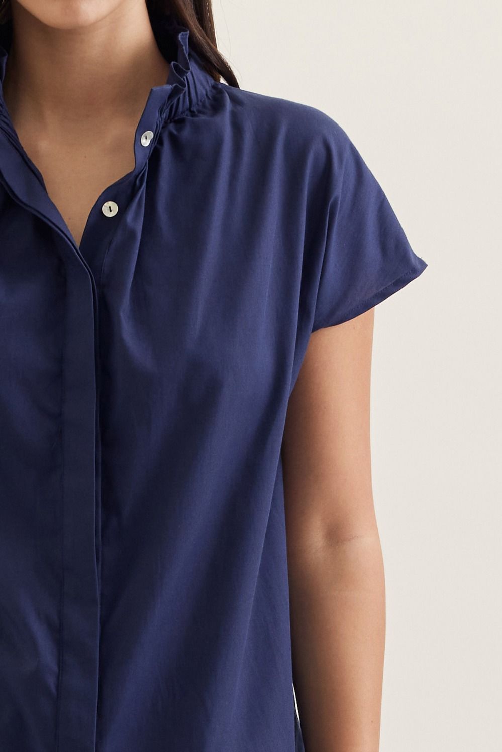 Aliana solid cap sleeve top in light beige with ruffled stand collar and button front closure.