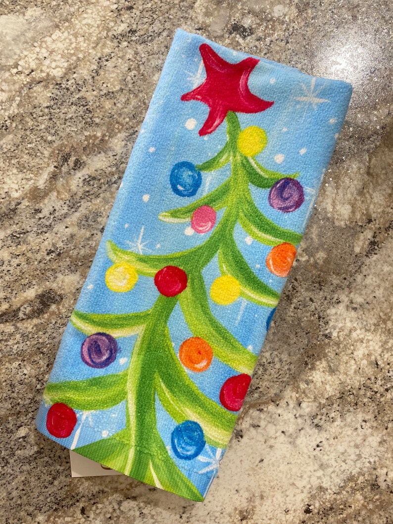 Holiday-themed tea towel with festive red and green patterns on a white background.