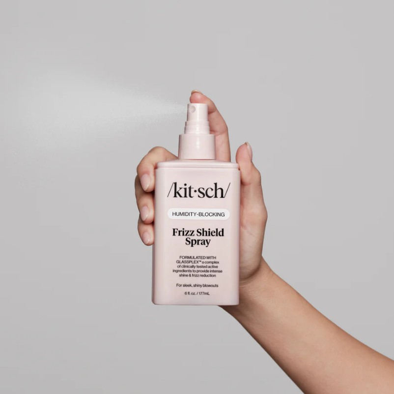 Hand holding a pink Kitsch Humidity-Blocking Frizz Shield Spray bottle while spraying a fine mist.