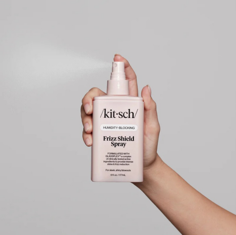 Hand holding a pink Kitsch Humidity-Blocking Frizz Shield Spray bottle while spraying a fine mist.