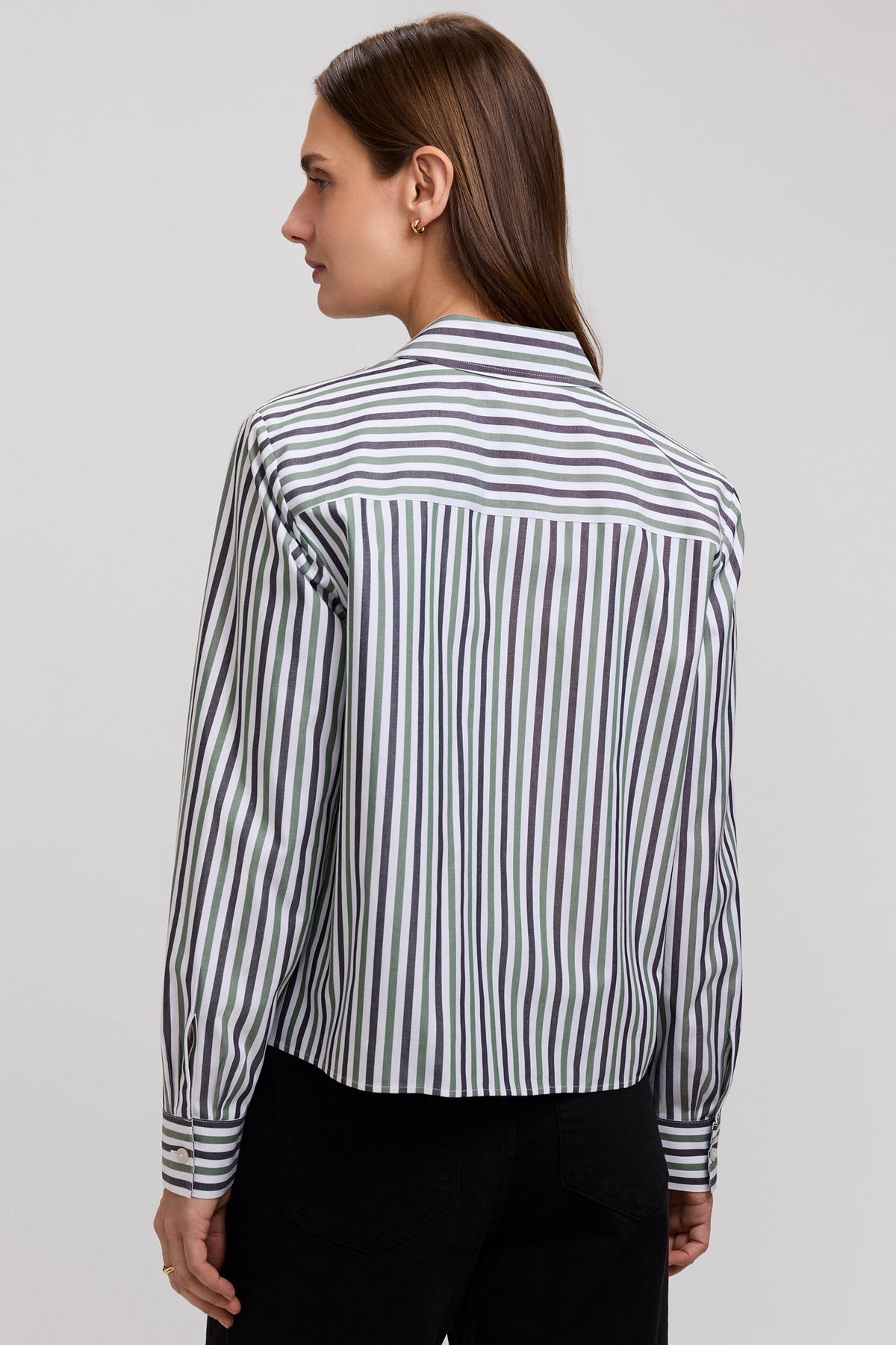 Back view of a woman wearing a green and white striped long sleeve button-up shirt and black pants.