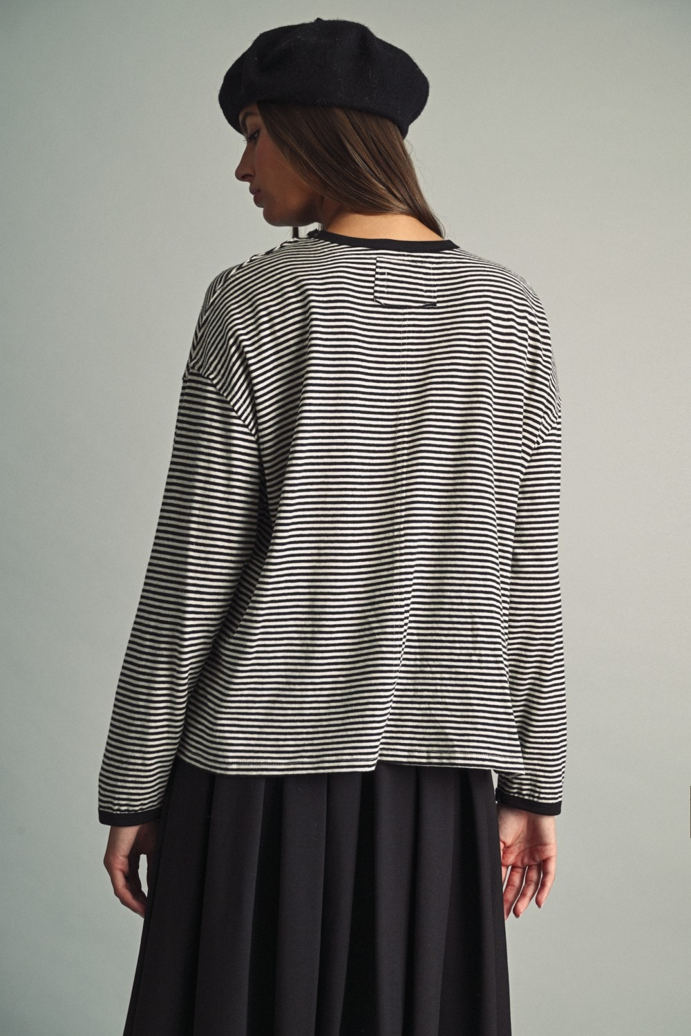 Back view of a woman wearing a black and white thin striped long sleeve top with a black beret.