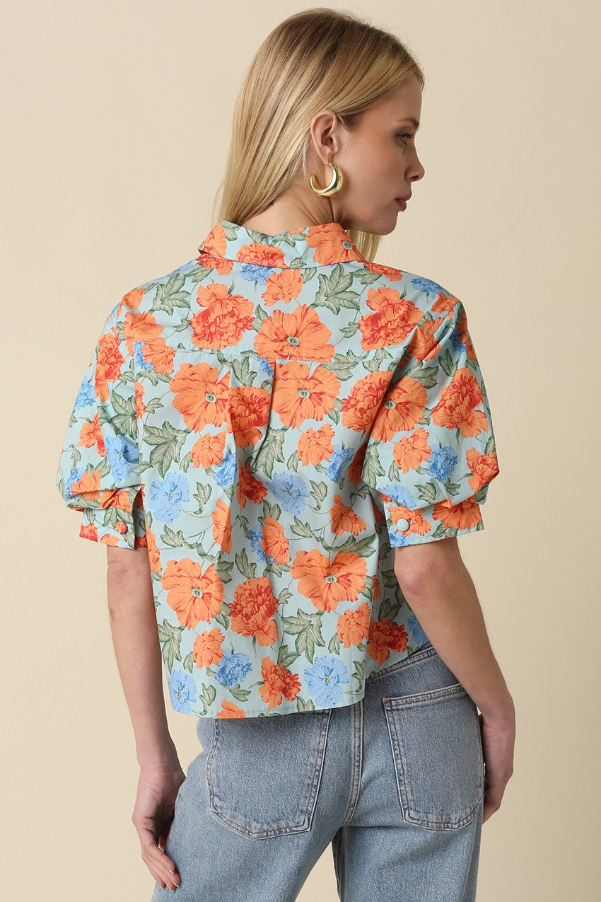 Back view of a woman wearing a light blue Mollie floral puff-sleeve button top with denim jeans.
