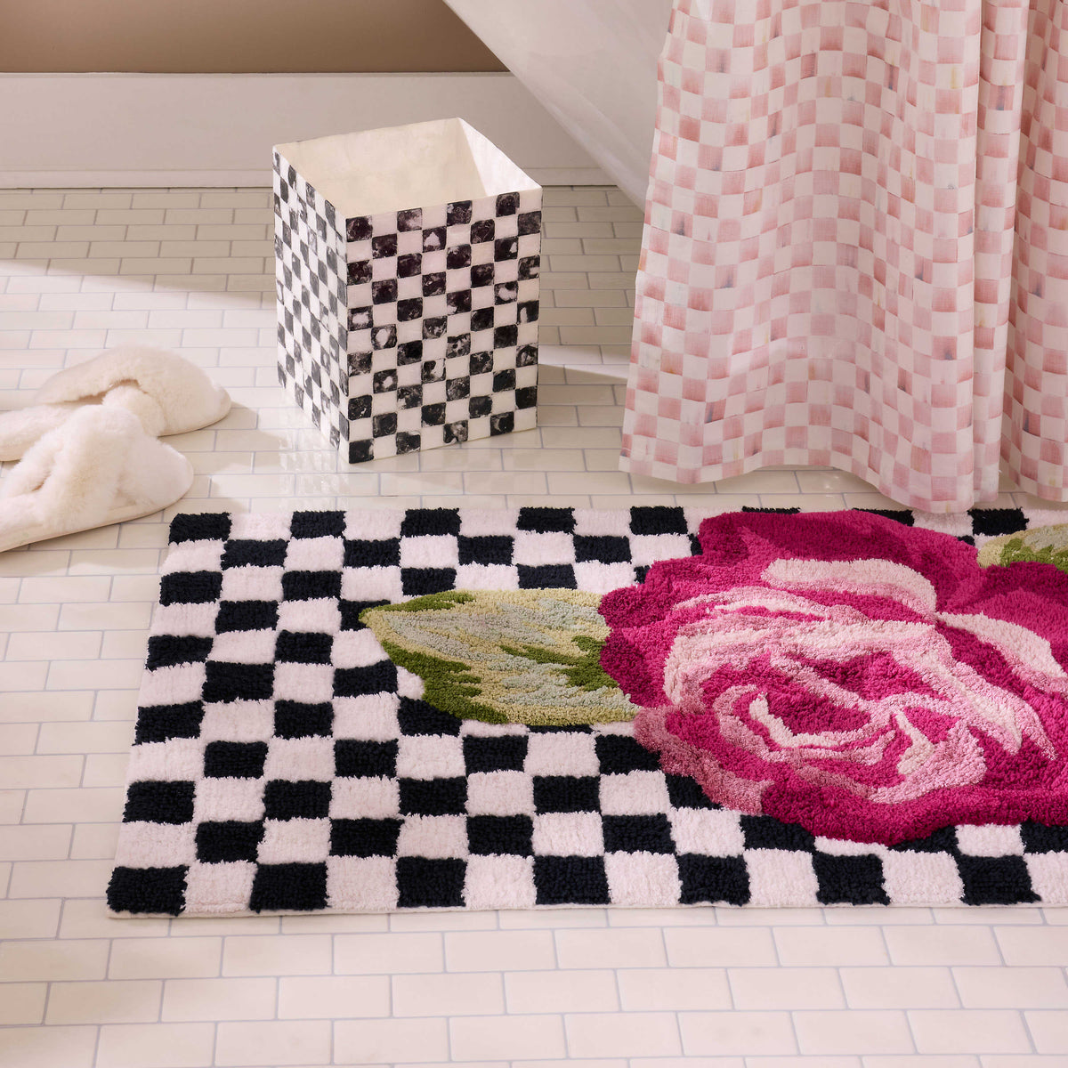 A rectangular bath rug with a black and white checkered pattern and a large pink rose design.