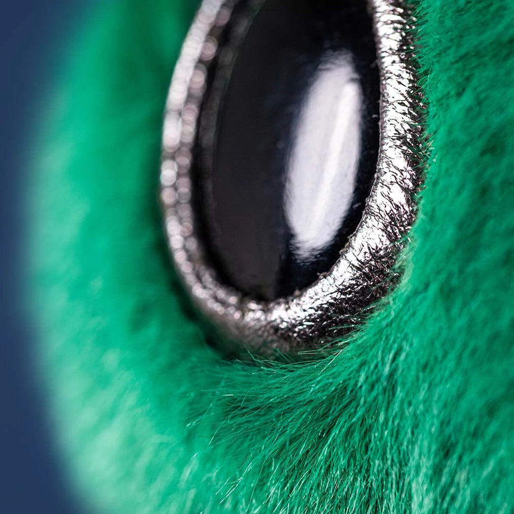 Close-up of the Zyllan Alien plush toy's shiny black eye with a silver rim and green faux fur.