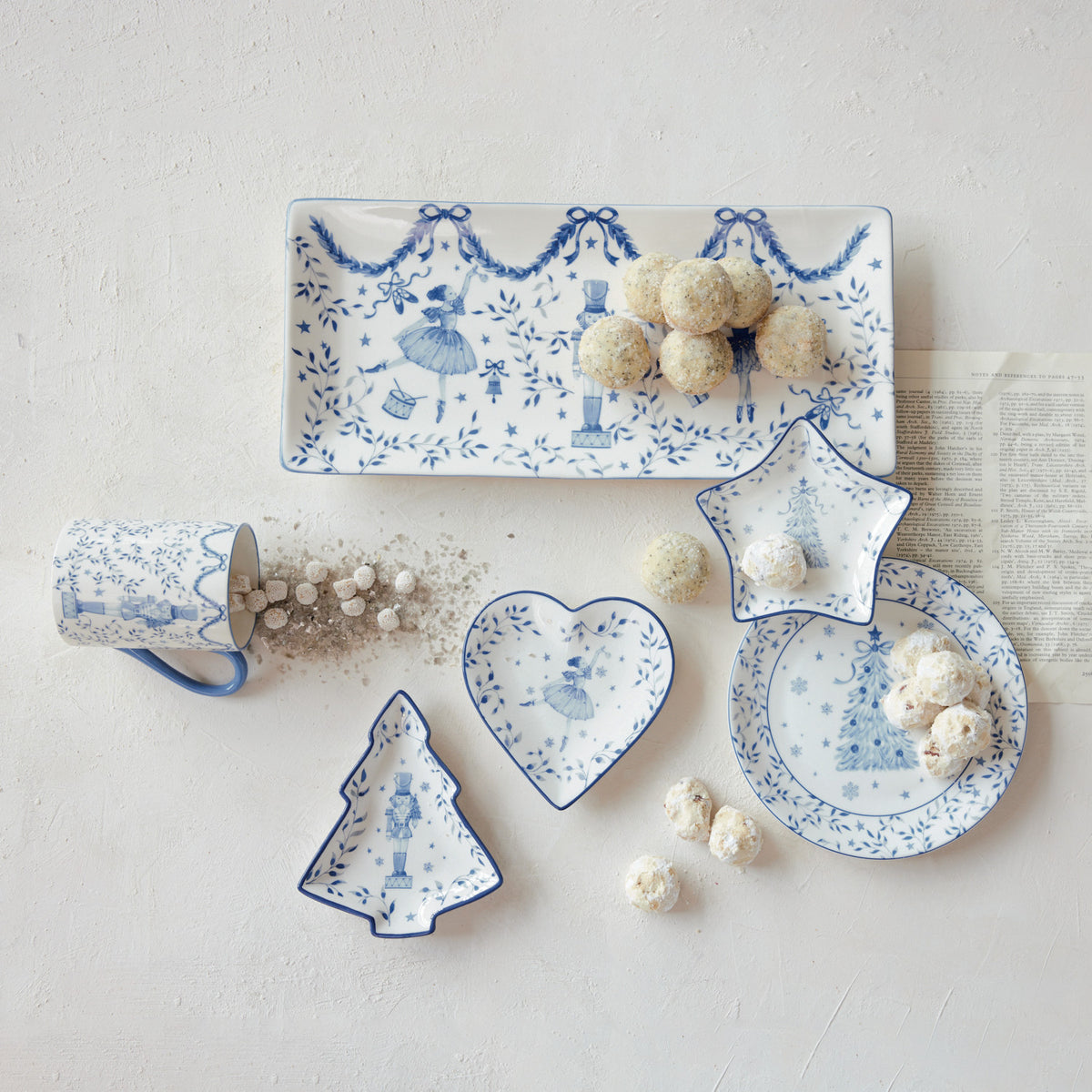 White and blue porcelain mug with nutcracker and ballerina illustrations on a table with dishes.