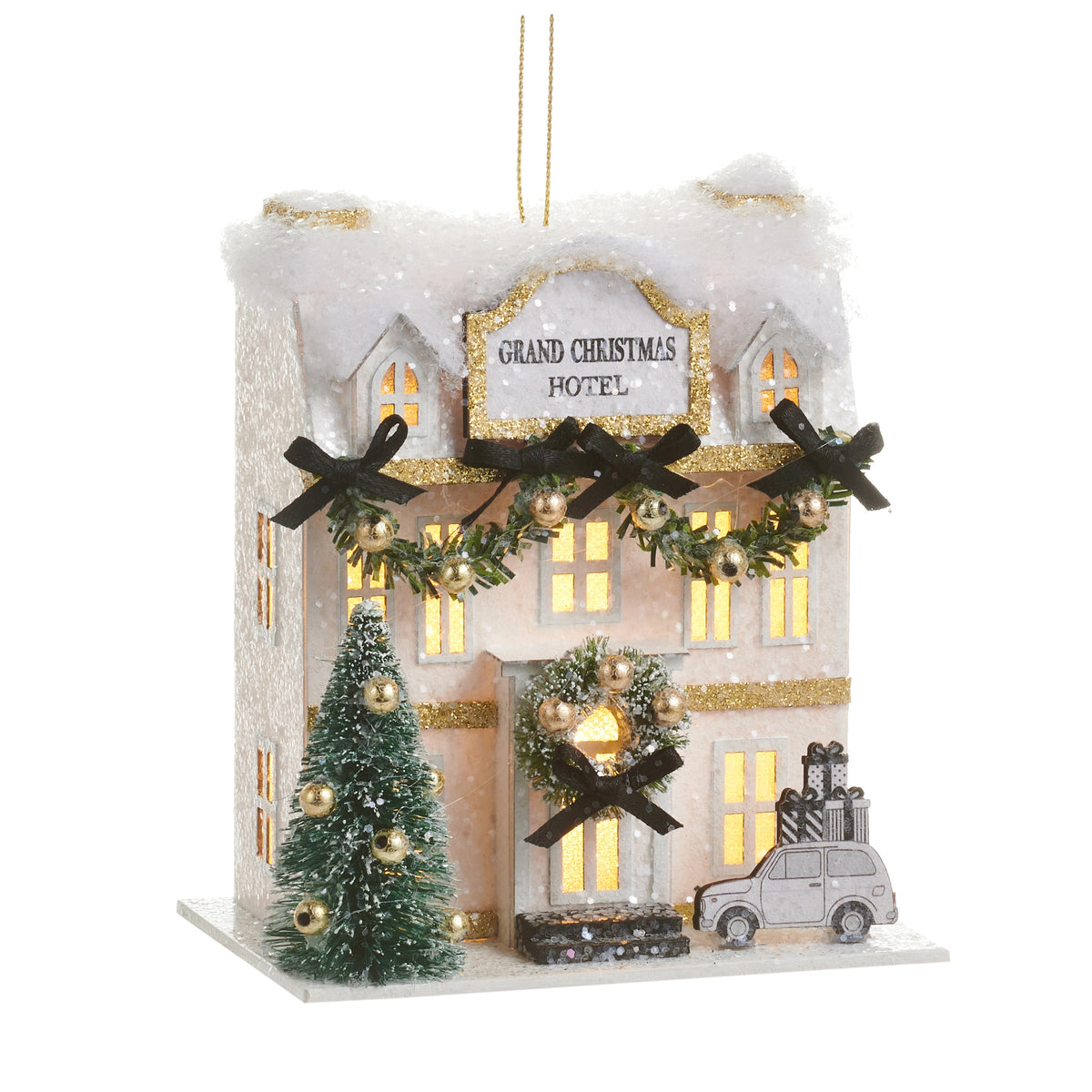 Lighted paper Christmas hotel ornament with snow-covered roof, wreaths, and a miniature car.