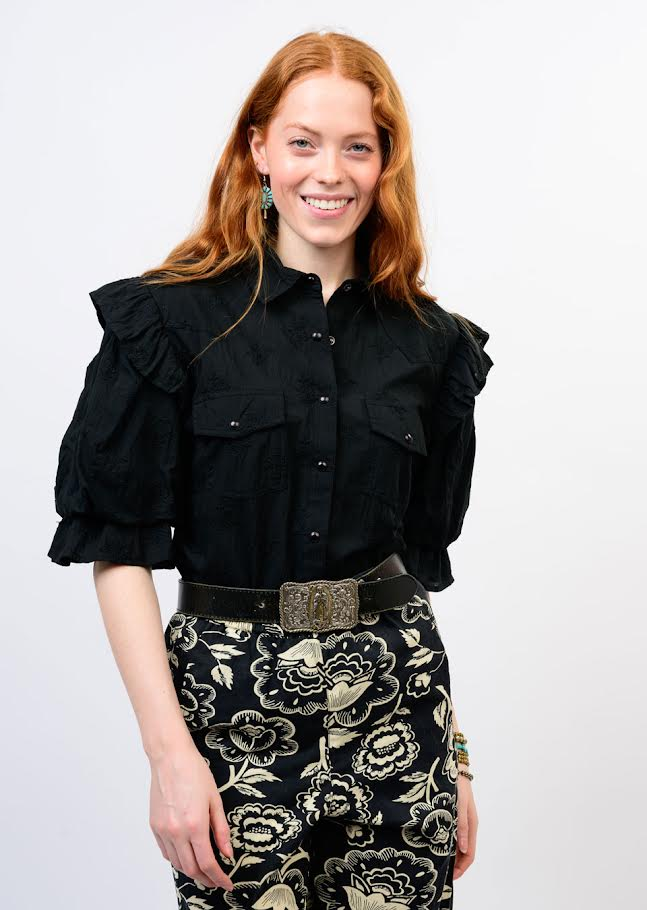 Woman wearing the Annie Top, a black button-down with ruffled shoulders and puff sleeves.