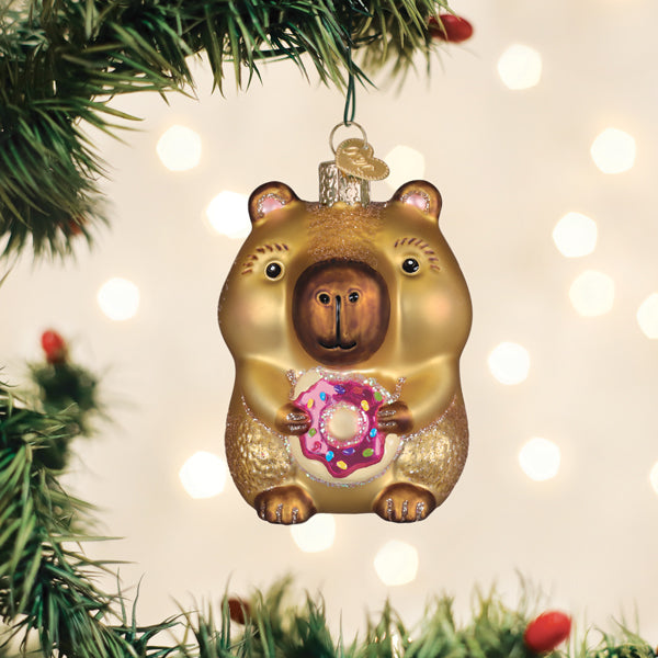 Capybara eating donut ornament in pastel pink with white polka dots on a gold rim