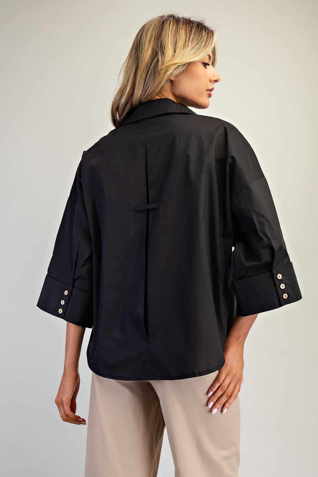 Back view of a black Blake blouse with three-quarter sleeves, buttoned cuffs, and center back pleat.