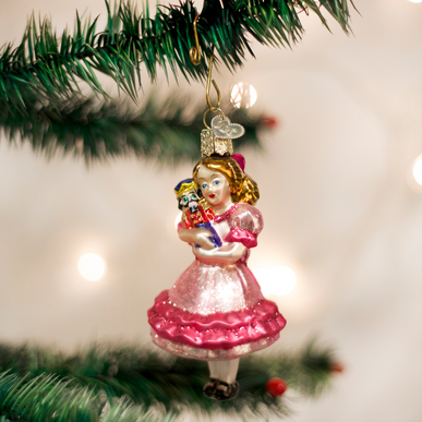 Clara glass Christmas ornament holding a nutcracker, hanging on a tree branch.